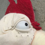 Eine Huhn-Handpuppe aus Schaumstoff in der Entstehung. Nahaufnahme mit Auge und Stecknadeln