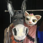 Handpuppen, ein Esel und die Katze hängen baumelnd an einer Kleiderstange. Zu dem Stück die Bremer Stadtmusikanten.