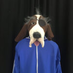 Die Hunde-Handpuppe mit Augenklappe, heraushängender Zunge, blauem Trainingsanzugs-Oberteil mit weissem Reissverschluss.